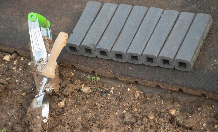 Close-up of a trowel and garden pavers next to soil in a garden setting.