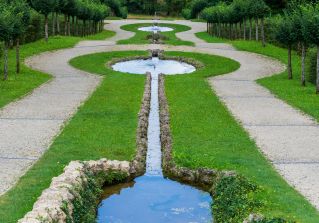 A peaceful green garden landscape with a symmetrical pathways and a reflective water channel.